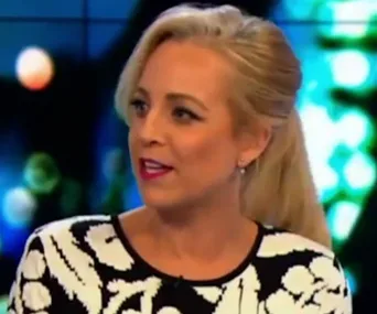 Person with blonde hair, in a patterned top, speaking emotionally on TV show.