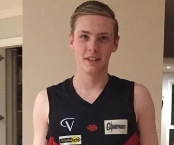 A person wearing a sleeveless sports jersey with sponsor logos stands indoors, smiling at the camera.