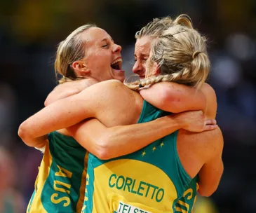 Australian netball players celebrate with a group hug after winning the World Cup, wearing green and yellow uniforms.