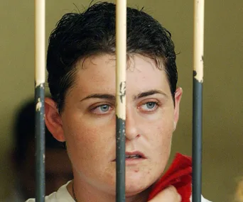 Person behind bars holding red cloth, gazing to the side.