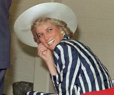 Princess Diana smiling, wearing a striped suit and wide-brimmed hat, hand near her face.