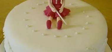 A cake with a fondant figure in a red dress sitting, surrounded by small decorative pearls.