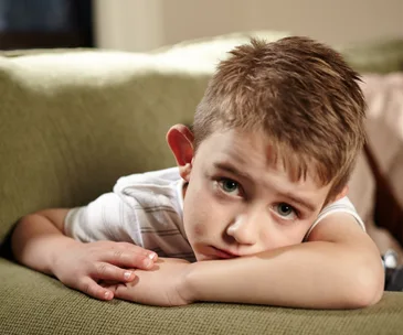 Young boy with short hair lying on a green couch, looking directly at the camera with a calm expression.