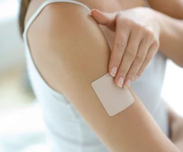 A person applies a nicotine patch to their upper arm.