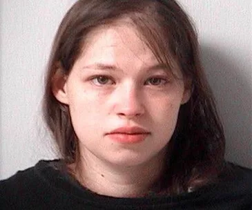 A woman with dark hair in a mugshot, wearing a black top, looking towards the camera with a neutral expression.