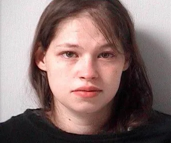 A woman with dark hair in a mugshot, wearing a black top, looking towards the camera with a neutral expression.