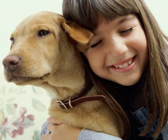 A smiling girl cuddles a tan dog, both appearing happy and content.