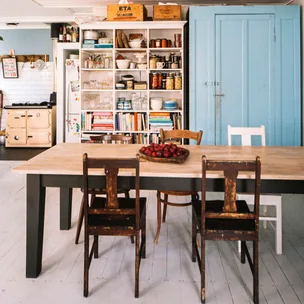 Cozy kitchen with wooden dining table, chairs, open shelves, books, jars, and a blue cabinet.