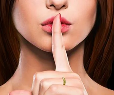 A woman with long hair has her finger to her lips, suggesting silence.