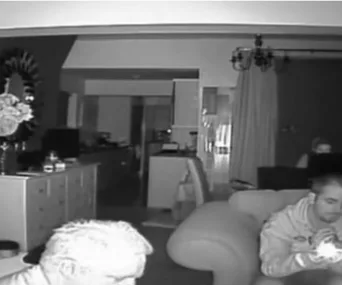 People sitting in a dimly lit room with a mirror and furniture visible in the background.