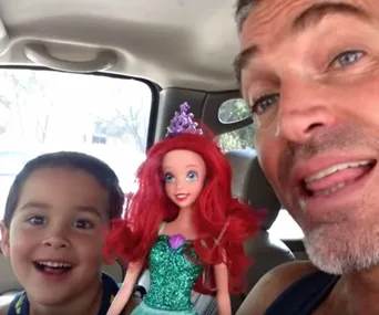 Father and son smiling in a car with a red-haired Ariel doll from "The Little Mermaid."