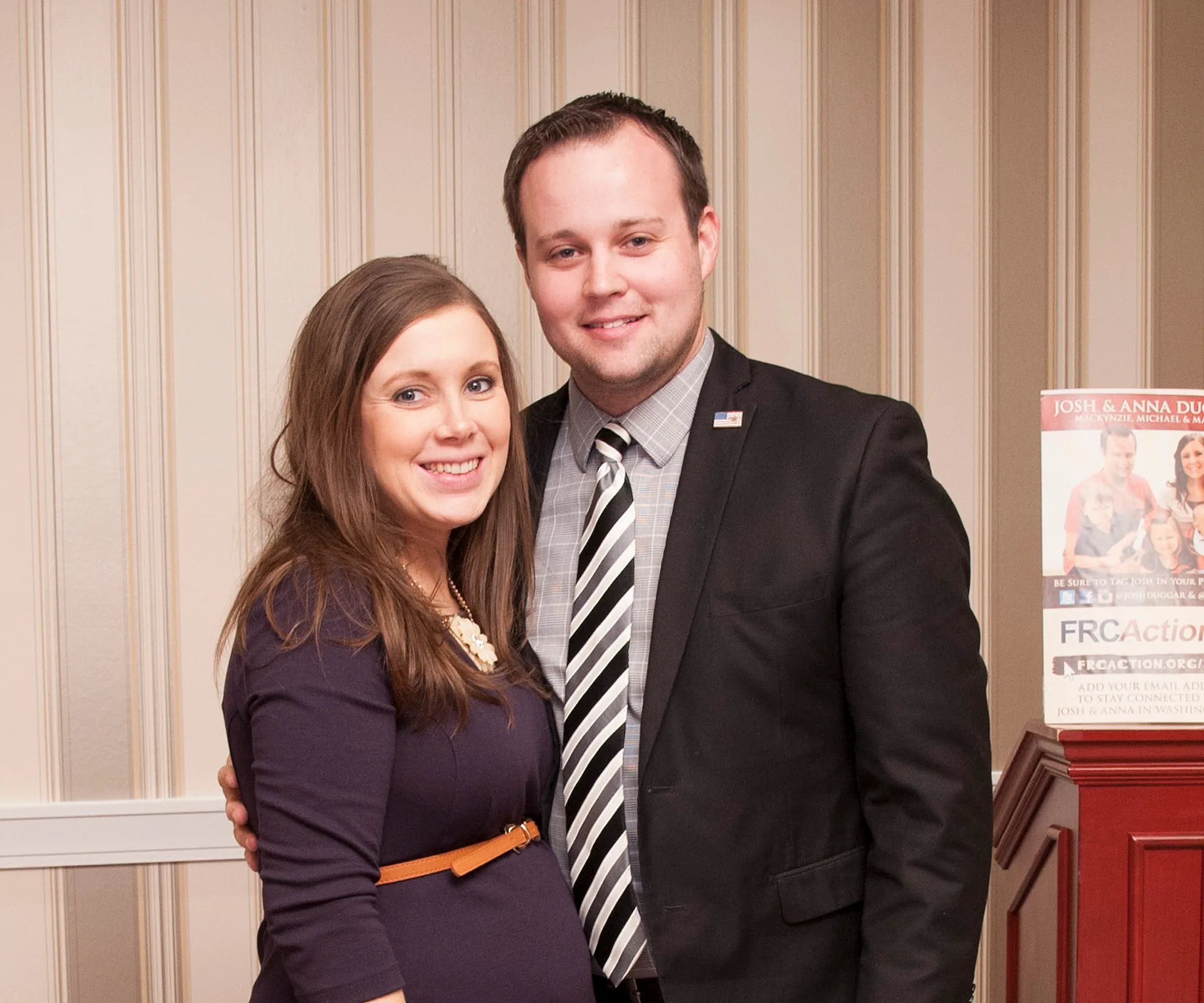 Couple smiling standing together indoors with striped wallpaper in the background.