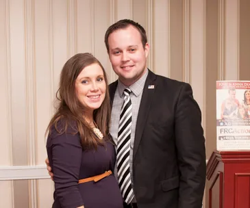 Couple smiling standing together indoors with striped wallpaper in the background.
