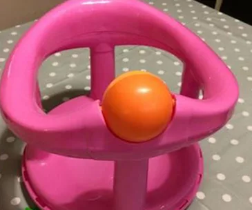 A pink baby bath seat with an orange ball, placed on a polka-dot surface.