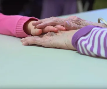 Child and elderly hands gently touching on a table, symbolizing connection between generations.
