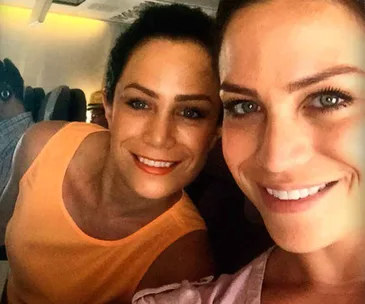 Two smiling women taking a selfie while seated on an airplane.