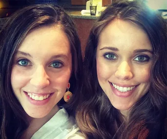 Two women smiling at the camera, indoors, with long hair and bright eyes.