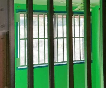 Green room with barred windows, resembling a cage, intended for secure confinement.