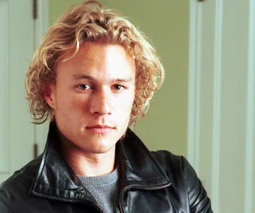 A person with wavy blonde hair in a leather jacket, looking directly at the camera.