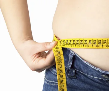 "Close-up of person measuring waist with yellow tape, wearing blue jeans."