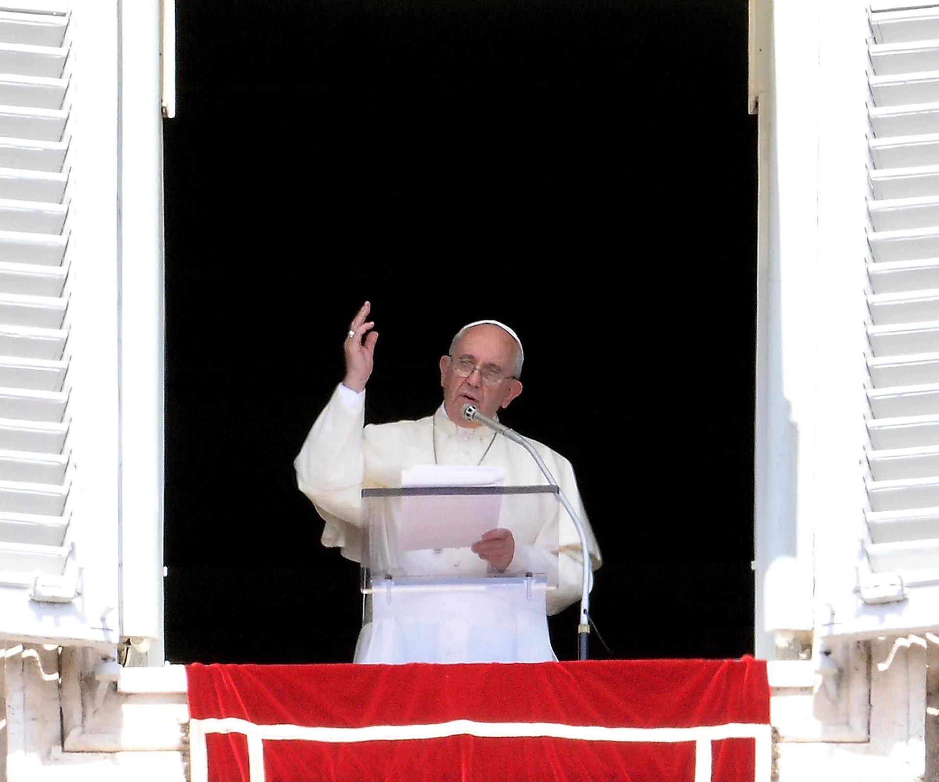 Pope delivering a speech from a window, gesturing with hand, wearing white robes and zucchetto.
