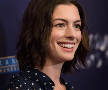 A smiling woman with shoulder-length hair in a polka dot shirt against a dark backdrop.