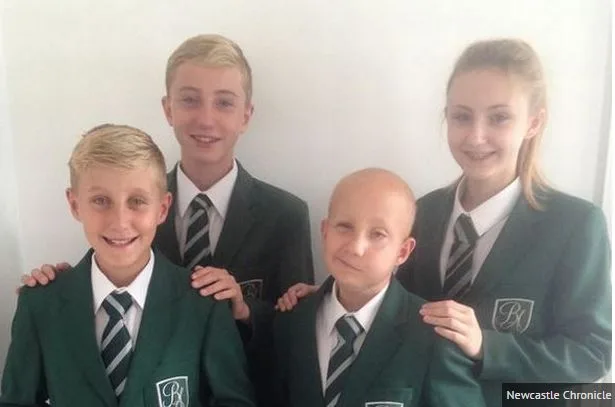 Four students in school uniforms smiling, with one in the front who is bald, indicating a brave cancer survivor.