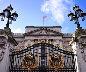 Buckingham Palace gates, adorned with gold detailing and the UK flag flying above the historic building.