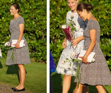 Crown Princess Victoria smiling in a patterned dress, holding flowers and a clutch, walking with another woman outdoors.