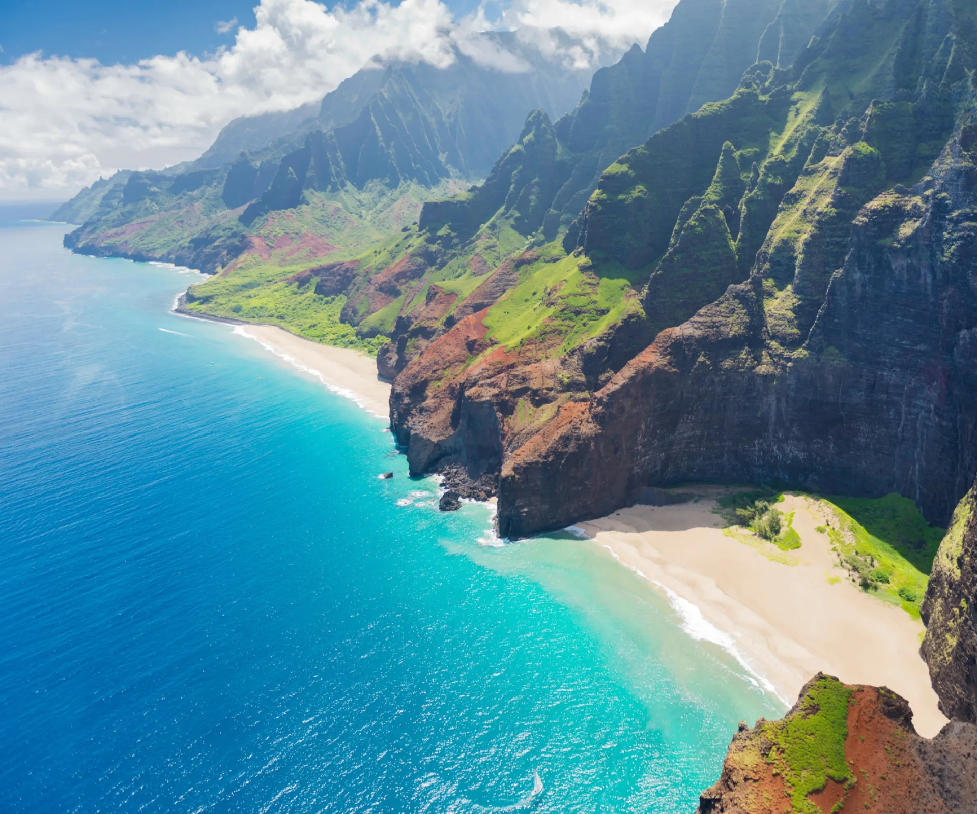 Aerial view of Na Pali Coast cliffs in Kauai, Hawaii, with blue ocean and sandy beach.