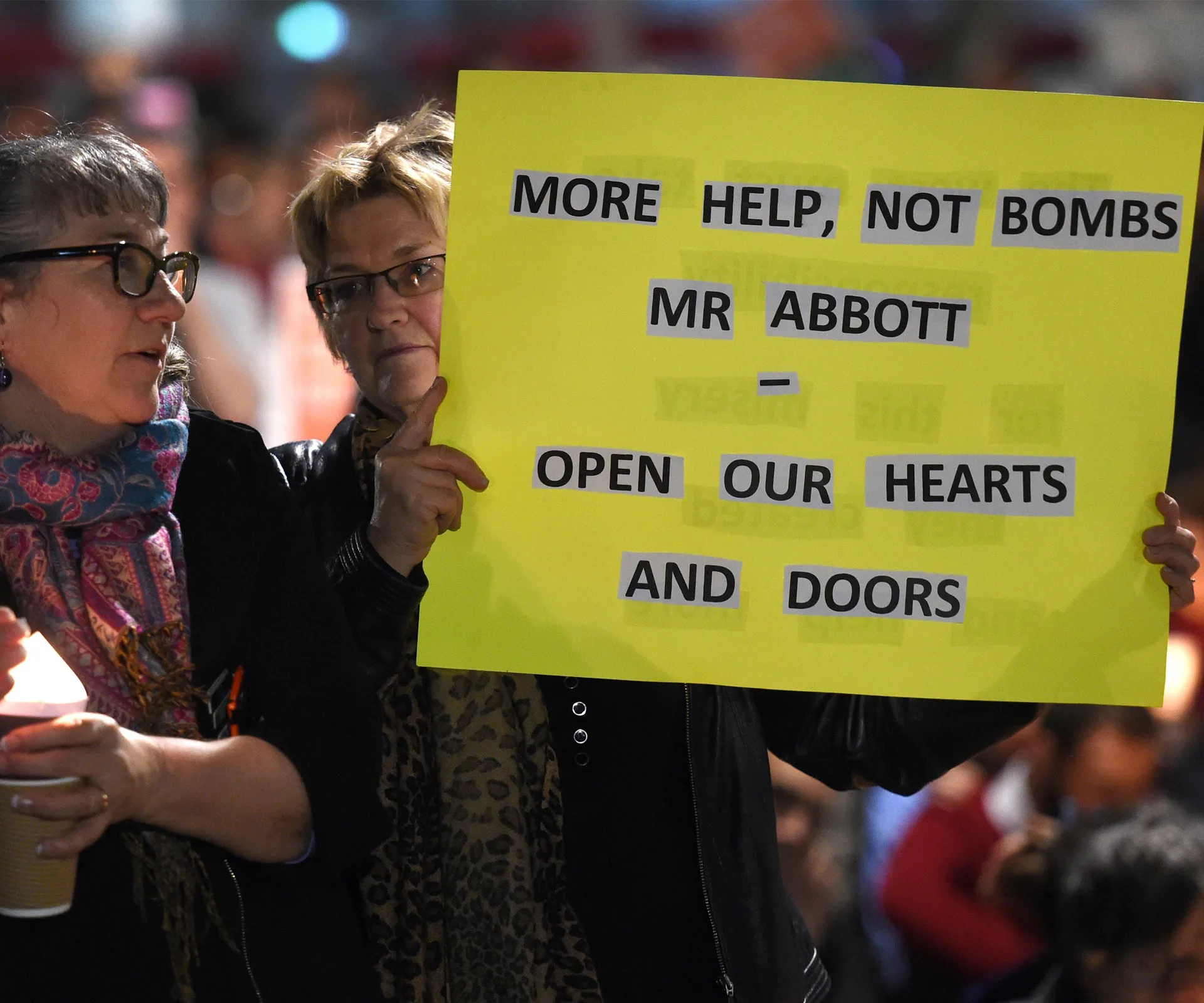 Two women hold a sign reading "More help, not bombs Mr Abbott – open our hearts and doors" at a protest rally.