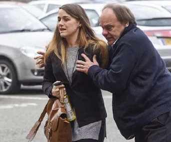 A woman walking with a bag, holding a drink, and a man beside her in a parking lot.