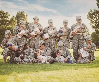 Soldiers in uniform seated and standing, breastfeed their babies outdoors.