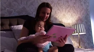 Mother reading a book to her toddler in a cozy bedroom setting.