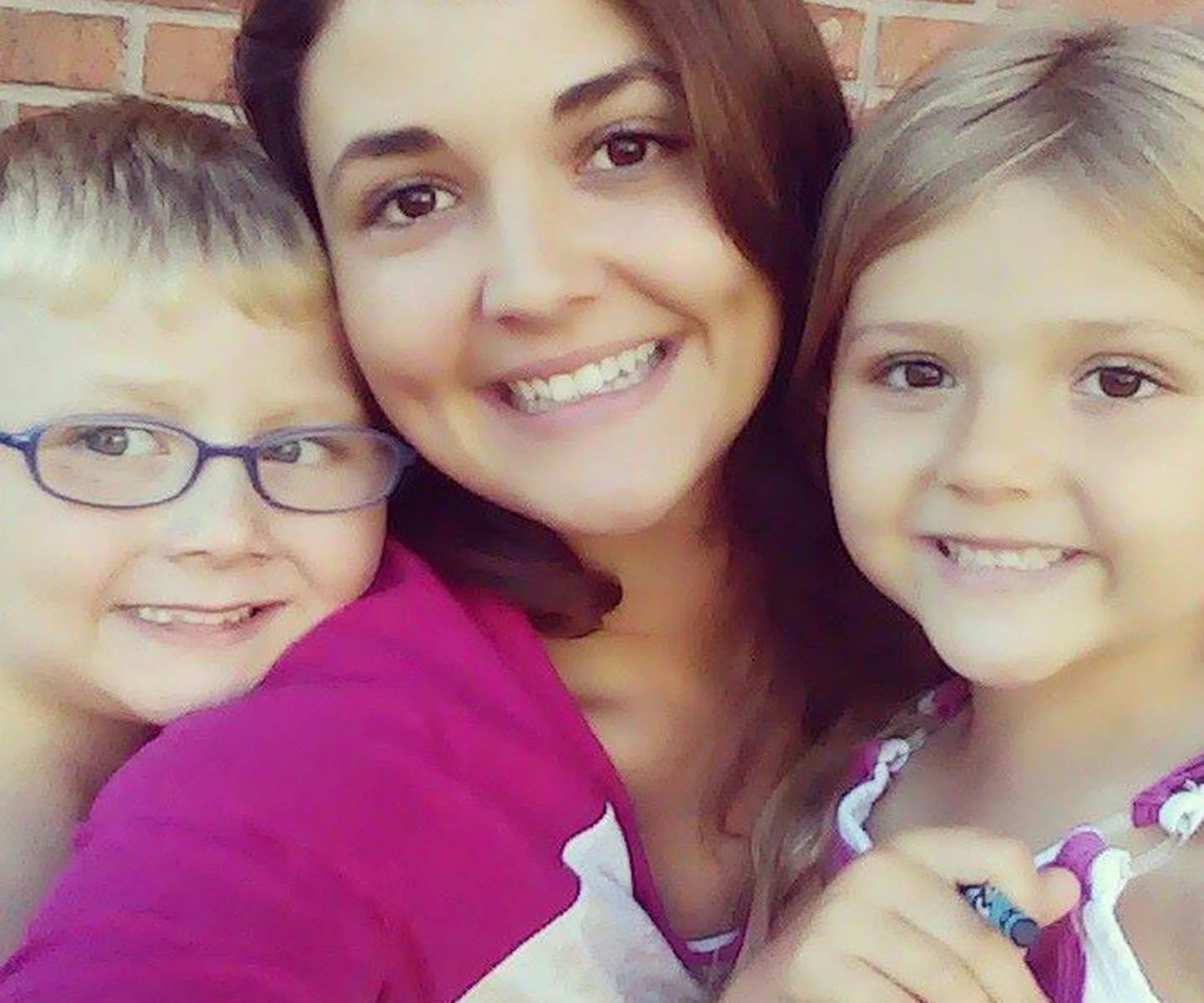 A woman and two children smiling together in a selfie.