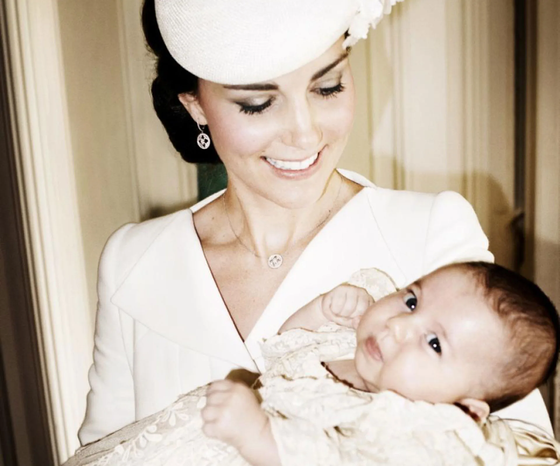 A woman in a white outfit smiling at a baby she is holding, both looking happy and content.