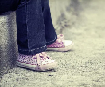Child wearing pink polka dot sneakers and jeans sits on a concrete step.