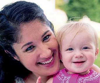 A smiling woman and baby, both looking at the camera, with a blurred green background.