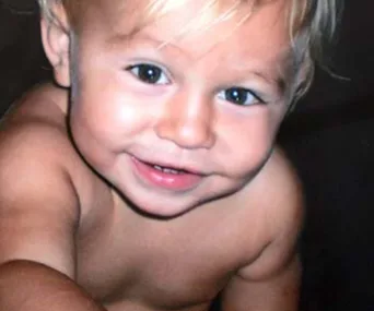 A smiling toddler with light hair, showing curiosity and joy.