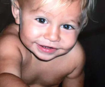 A smiling toddler with light hair, showing curiosity and joy.