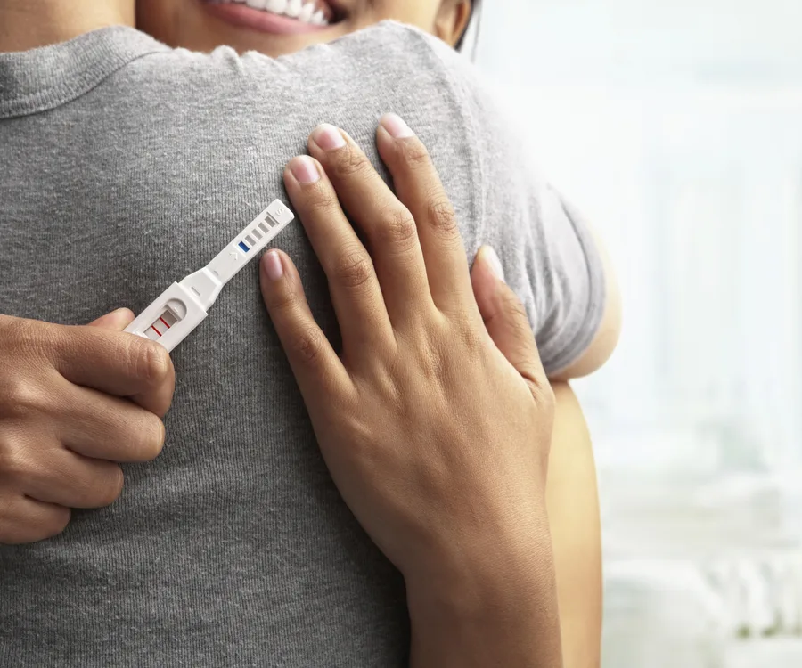 A person holds a positive pregnancy test while hugging another person.