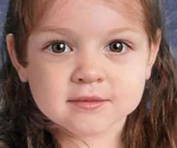 Young child with long brown hair and deep brown eyes gazing at the camera, set against a subtle blue background.