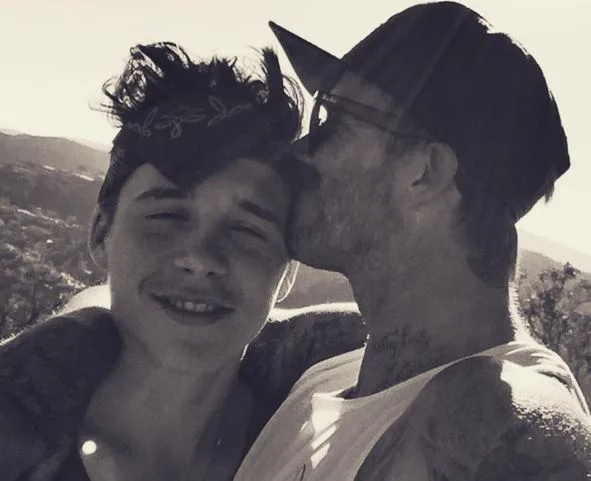 Father kissing son's forehead in outdoor setting, with the sun casting a warm glow.