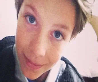 A young boy smiling at the camera, with blue eyes and short hair, looking slightly upwards.