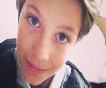 A young boy smiling at the camera, with blue eyes and short hair, looking slightly upwards.