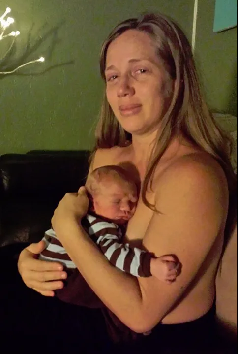 A mother lovingly holds her newborn, sitting in a dimly lit room.