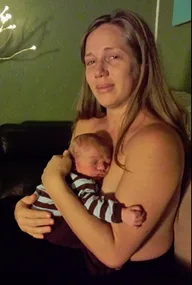 A mother lovingly holds her newborn, sitting in a dimly lit room.