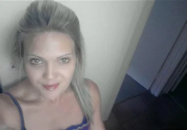 A woman with long blonde hair in a blue top stands in a doorway, looking up at the camera with a neutral expression.