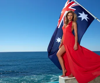 Woman in red dress poses by ocean with Australian flag.