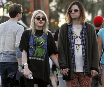 Two people holding hands at an outdoor event, wearing sunglasses and casual attire.